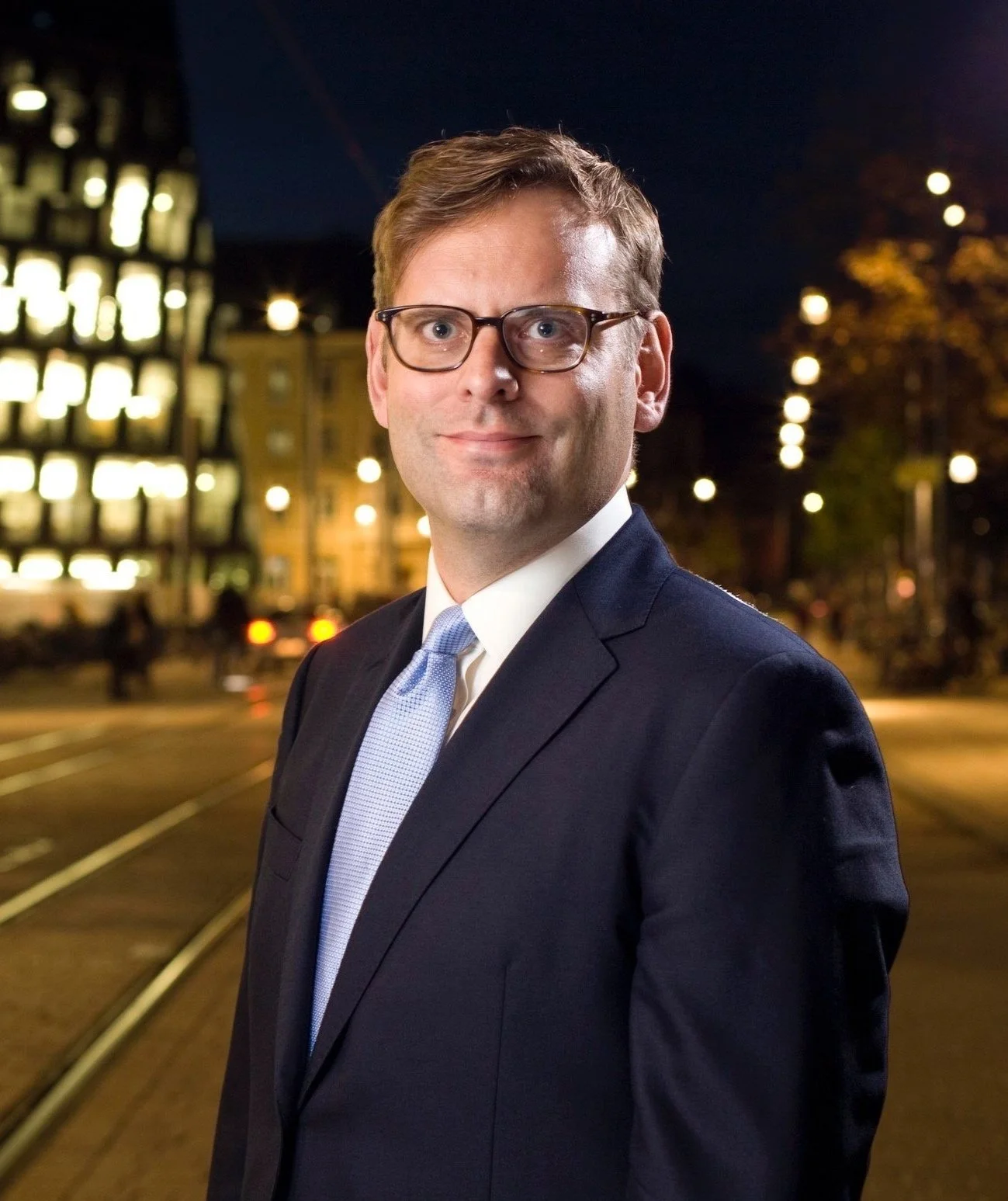 Mann im Anzug vor beleuchteter Stadtlandschaft bei Nacht