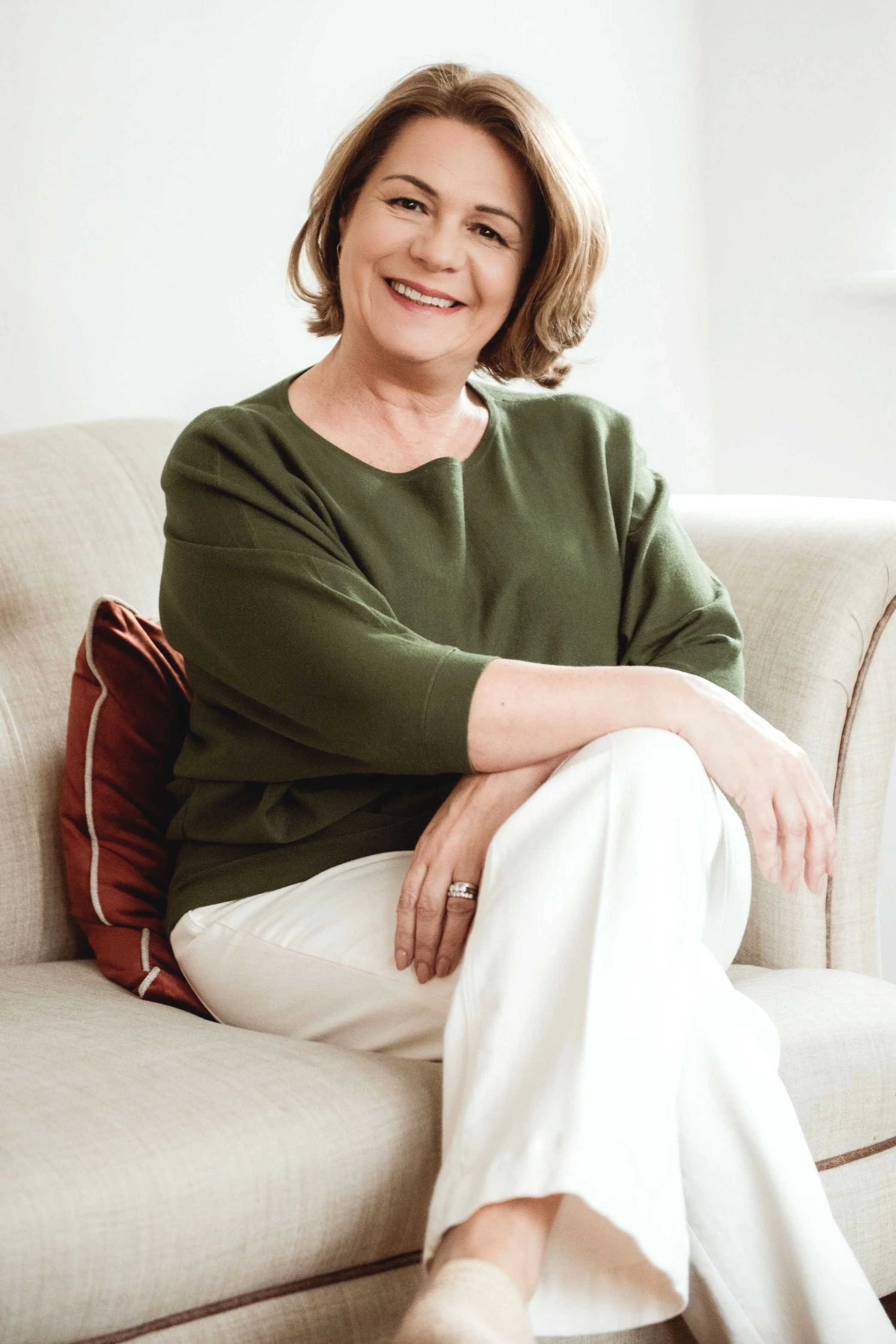 Therapist Lois Dabrowski from Limen Therapy wearing a green top and sitting on a sofa with legs and arms crossed, smiling