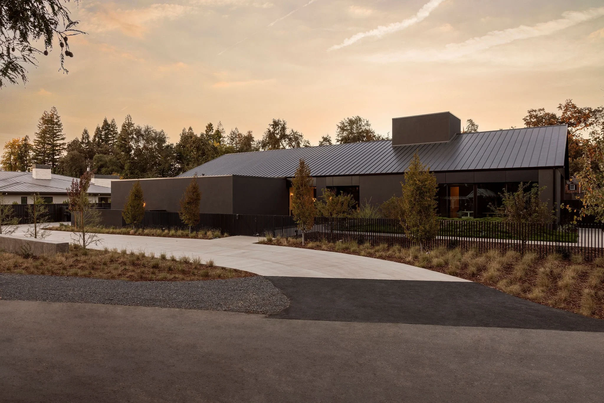 Modern home from exterior, metal roof, dark stucco siding, sunset