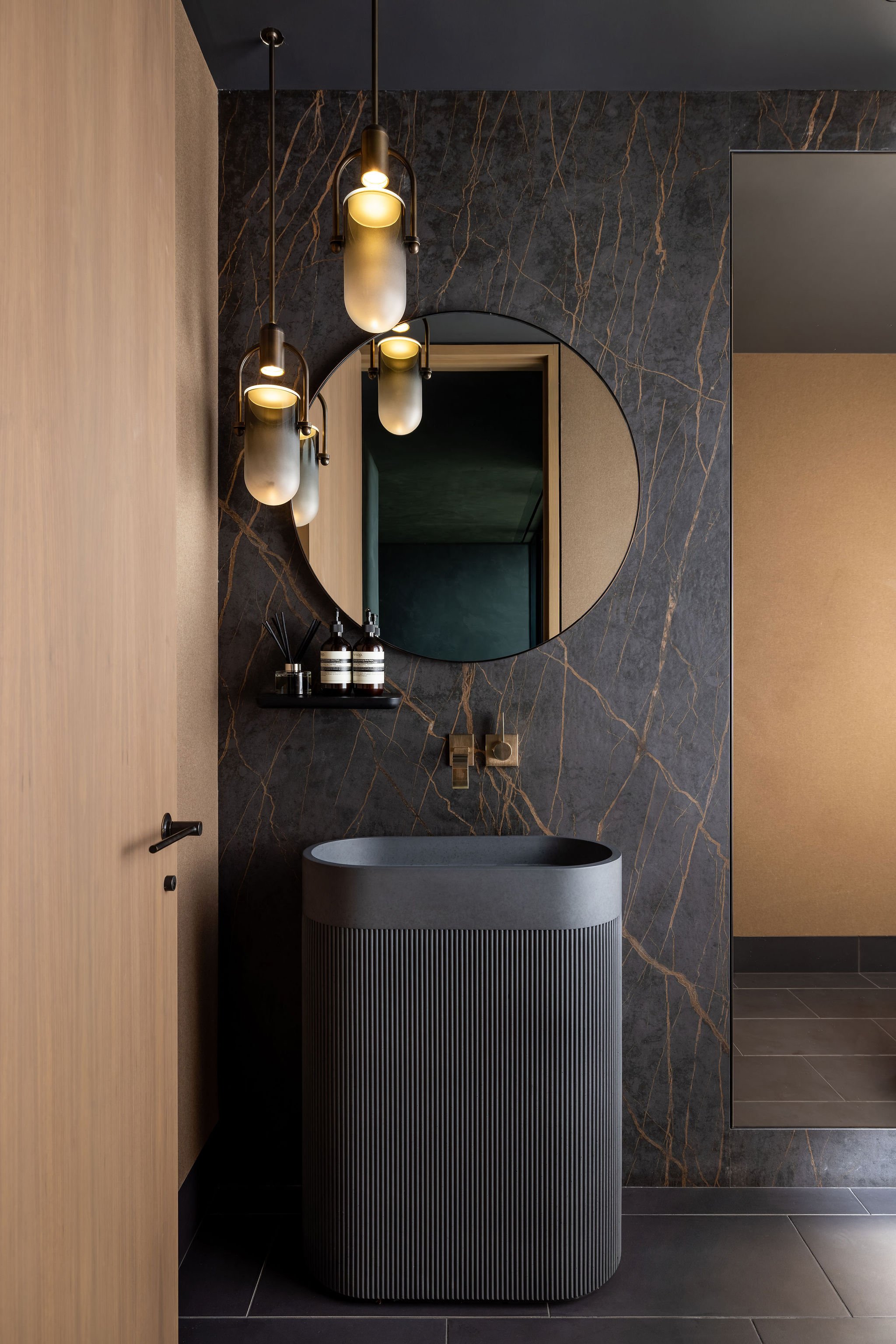 Modern, dark, moody powder bath with pedestal sink and mirrored cabinetry set flush with Dekton stone wall cladding