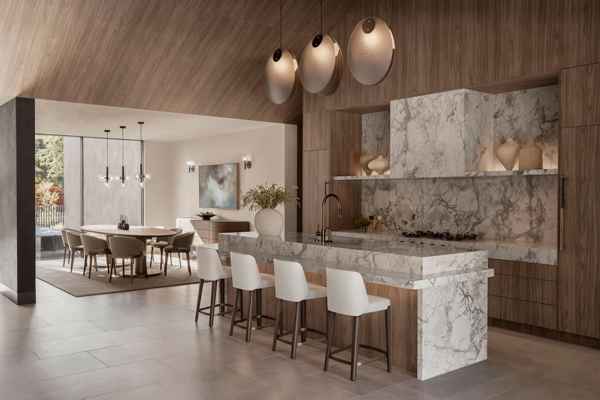 Modern European style kitchen in great room with vaulted, cabinet panel clad ceilings and island surrounded in stone. Dining room set off to side of kitchen