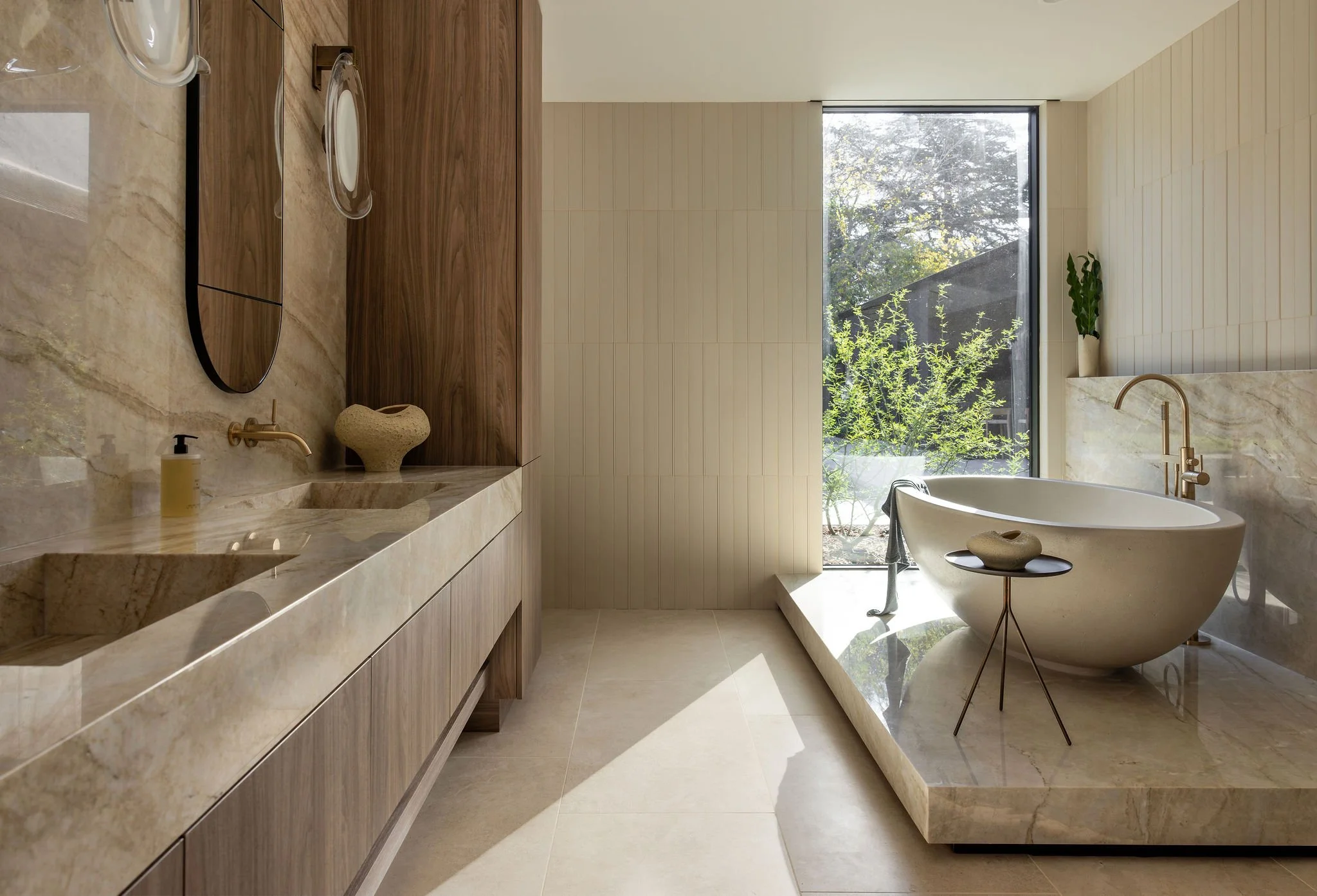 Modern primary bathroom with floating cabinet vanity, double sinks, freestanding stone tub on a stone pedestal