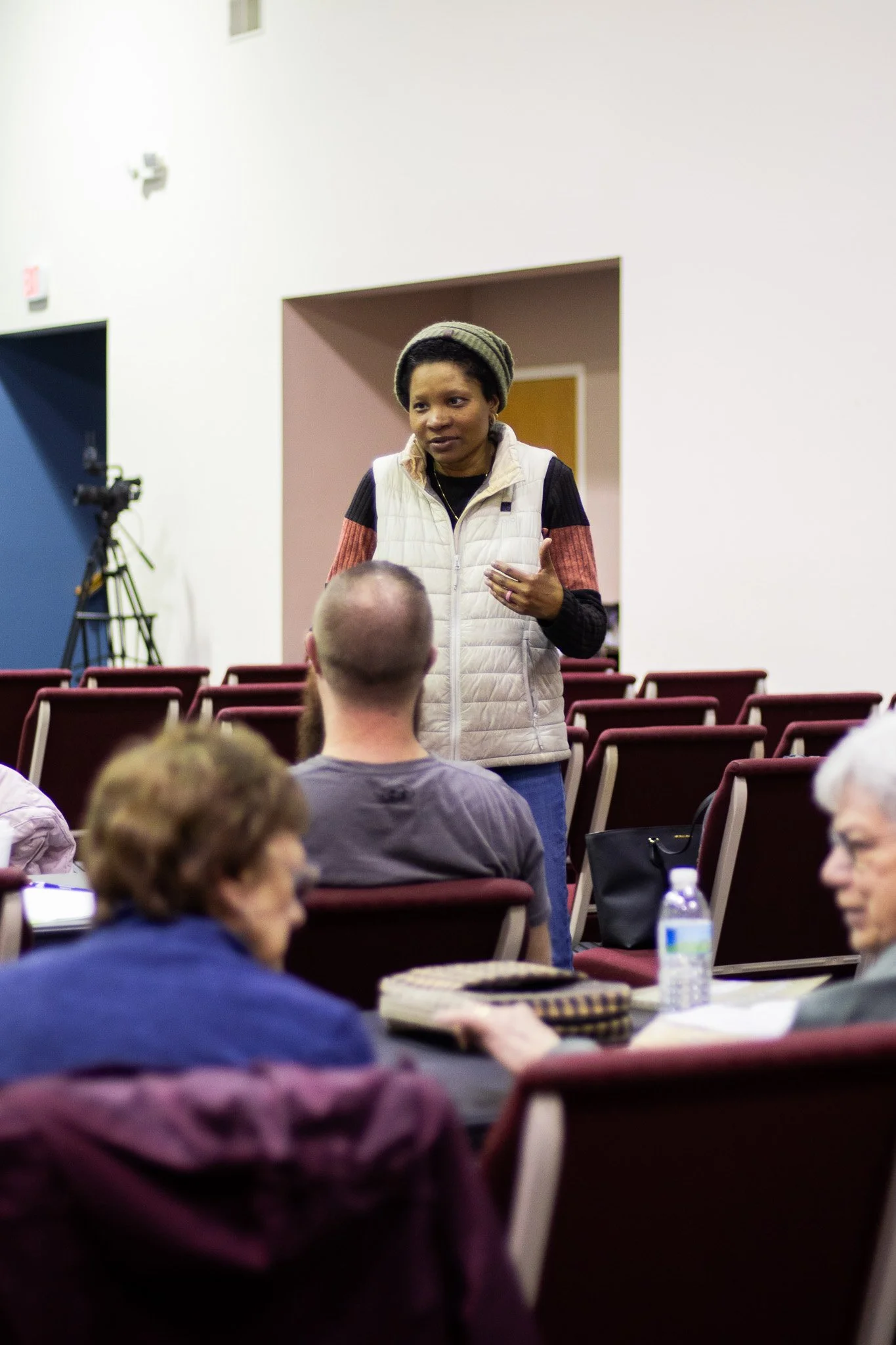 People standing with some raising their hands in a church or conference room during a gathering or service, with a large screen displaying lyrics or text at the front.