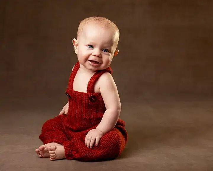 Portrait  of baby sitting in red woollen dungarees