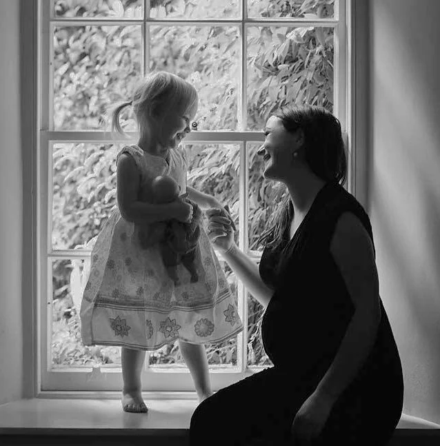 Black and white portrait of mother and young daughter by a window