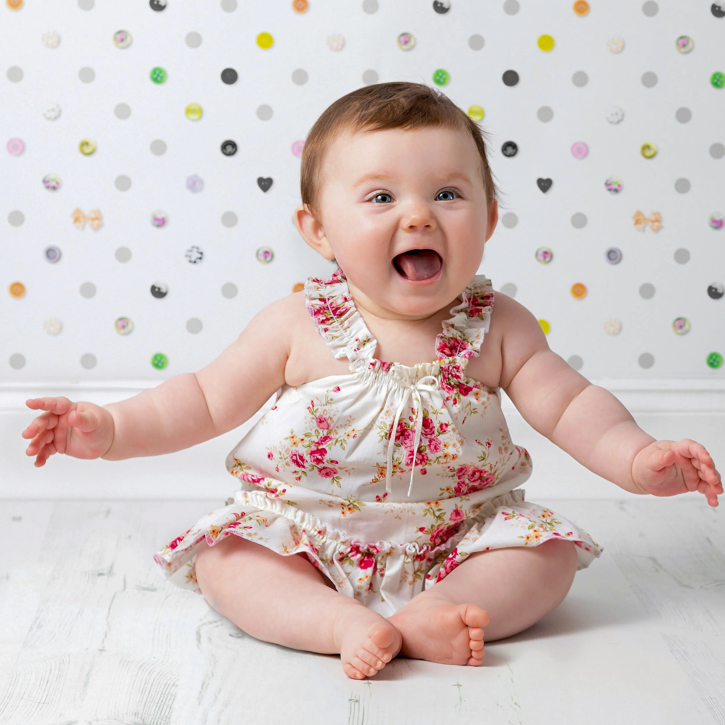 Baby sitting in a floral dress against a patterned backdrop