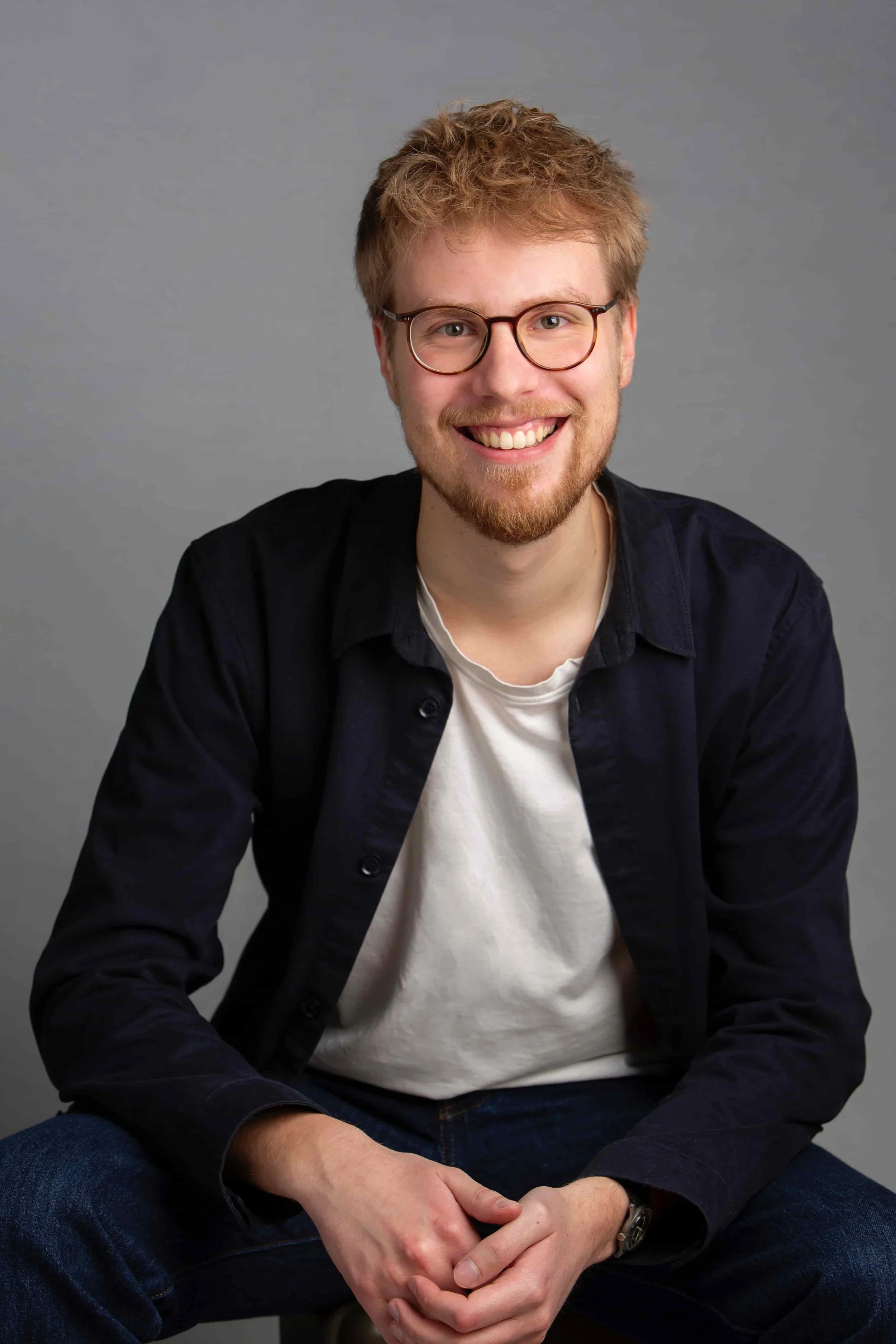 Finn Hendrik Baumann sitzt lächelnd vor einem grauen Hintergrund.