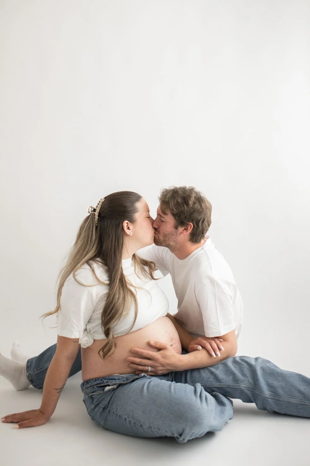 mom and dad studio maternity photos wearing white shirts and blue jeans