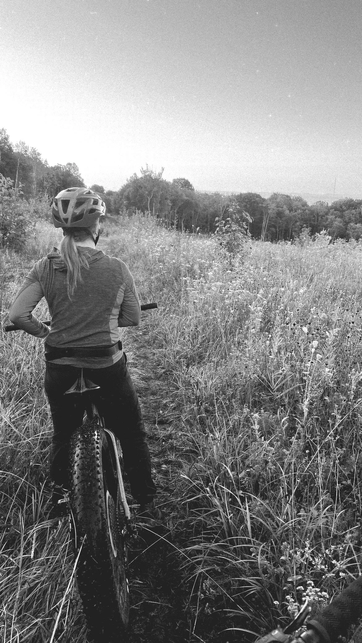 A person riding a mountain bike through a grassy trail in a natural outdoor setting, wearing a helmet and long sleeves.
