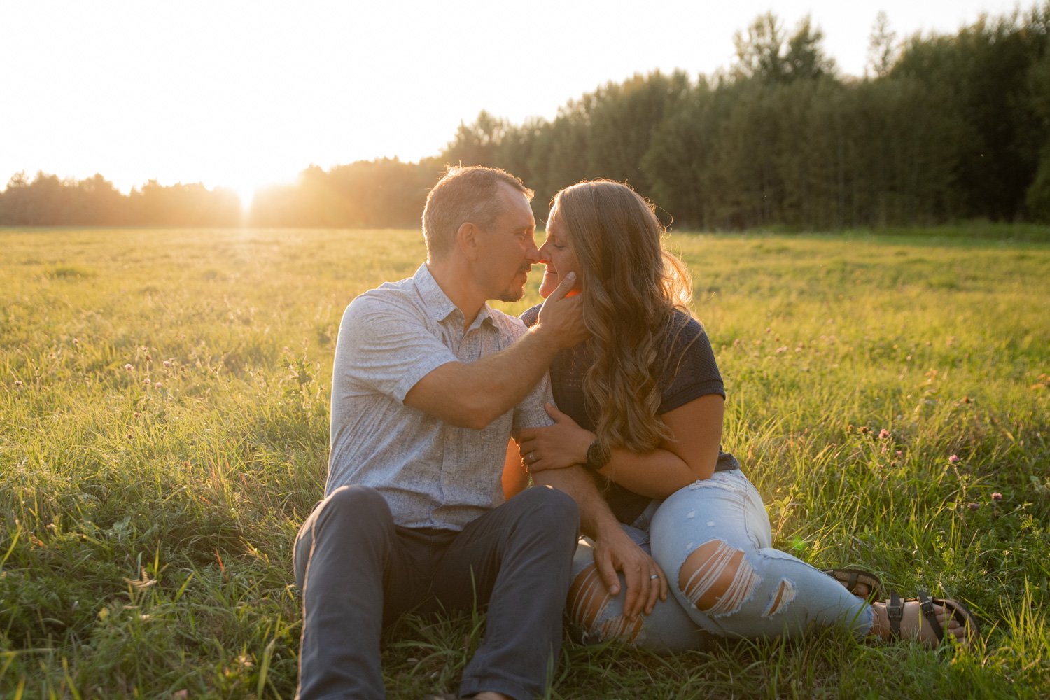 couple sitting in a field snuggling at sunset