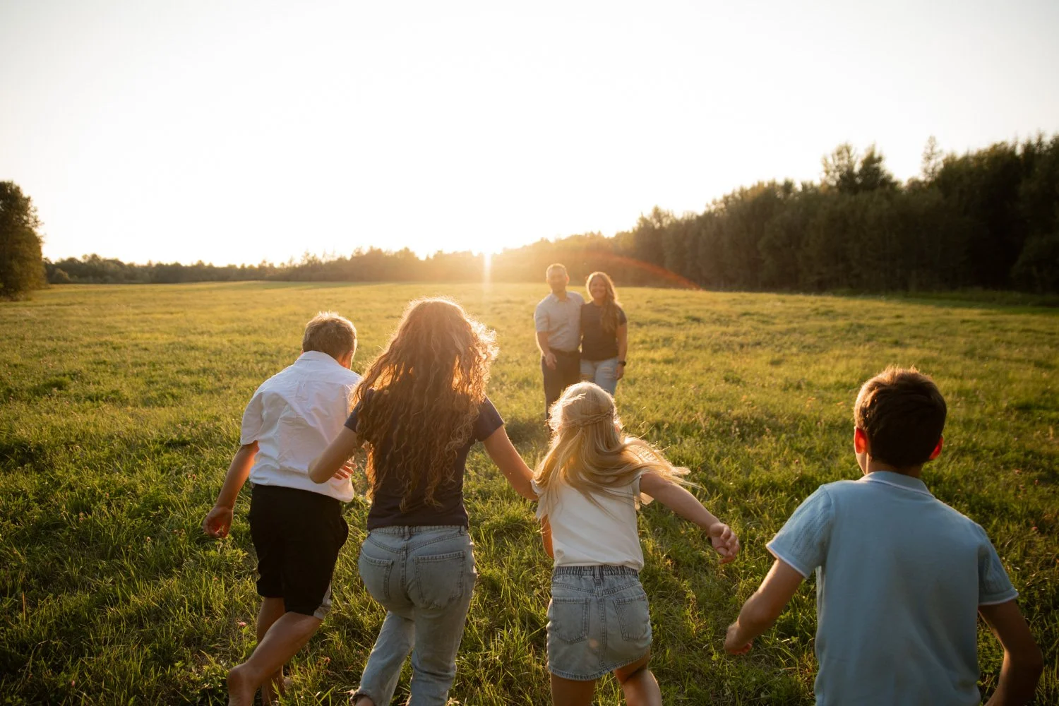 large family running to mom and dad in a field at sunset photoshoot