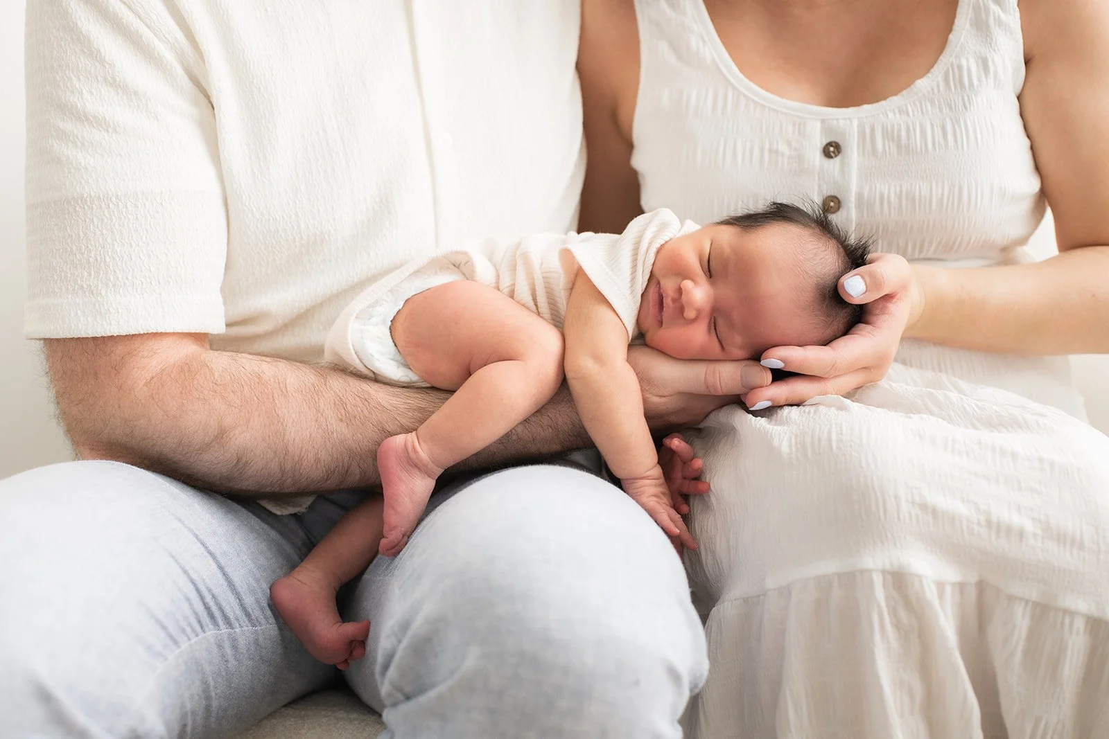 newborn baby on mom and dads lap sleeping studio photography