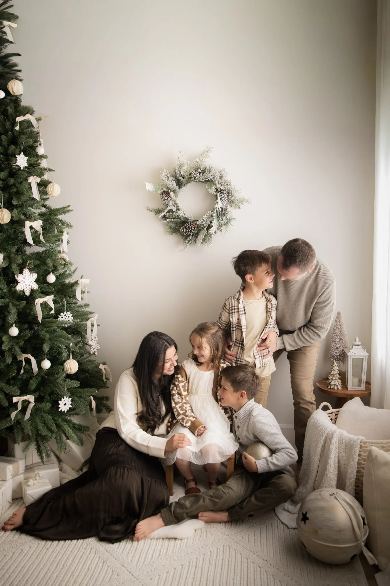 Family Christmas portrait in a bright photography studio with a decorated tree, soft textures, and warm holiday tones