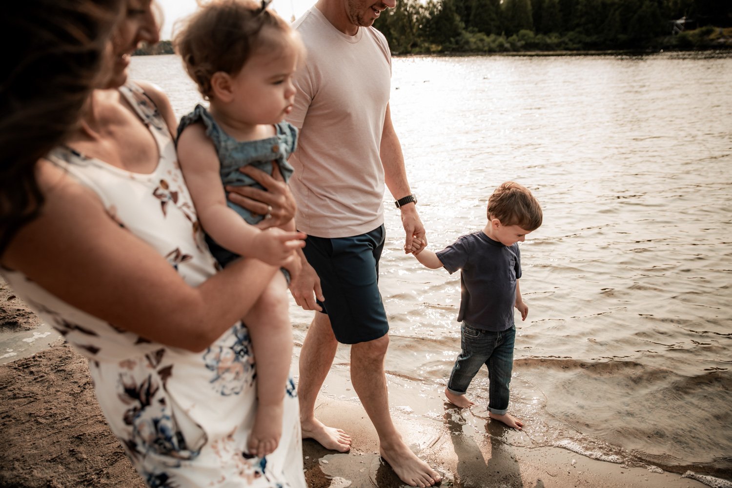 Family on the beach, holding hands, with a young boy walking into the water, during sunset.