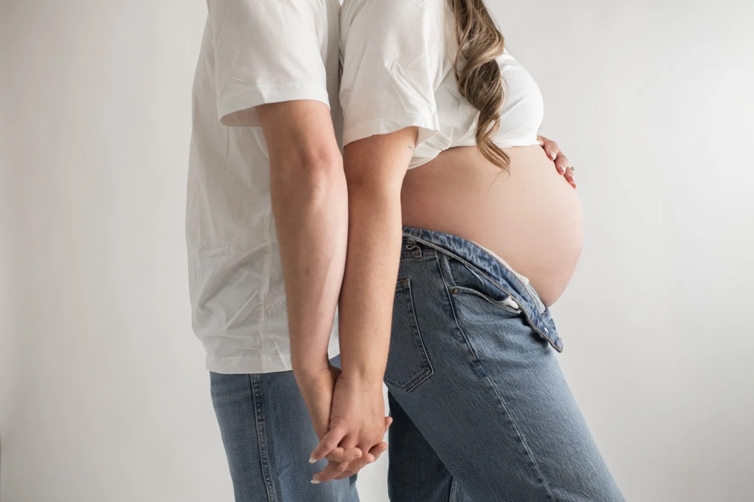mom and dad studio maternity photos wearing white shirts and blue jeans
