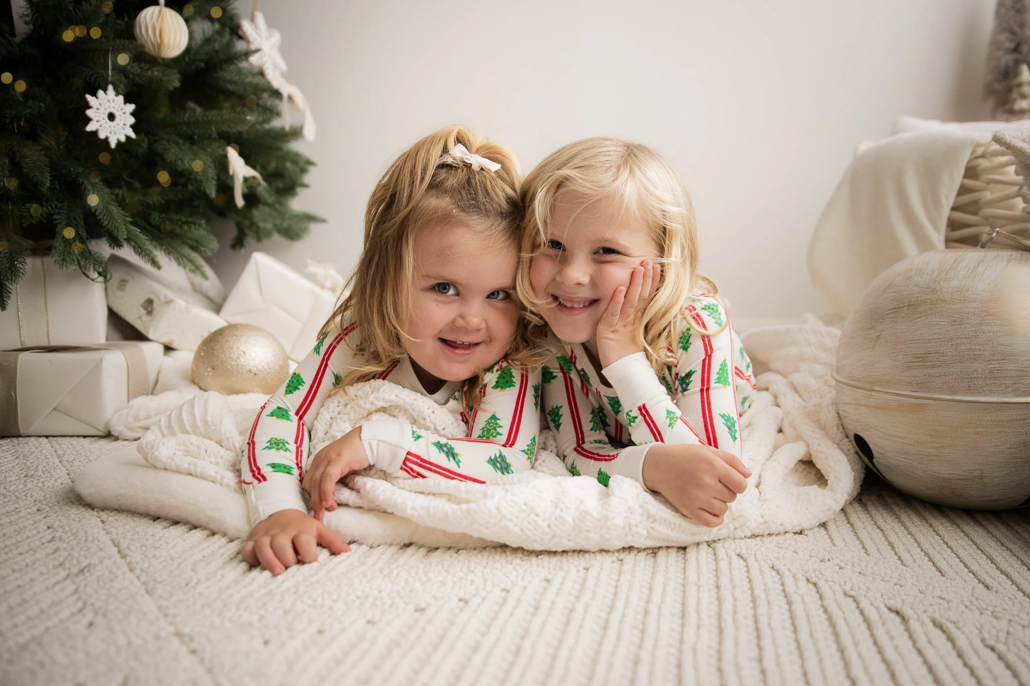 Sisters cuddled in festive holiday pajamas during a studio Christmas Minis Kids Edition photoshoot, surrounded by minimal Christmas décor