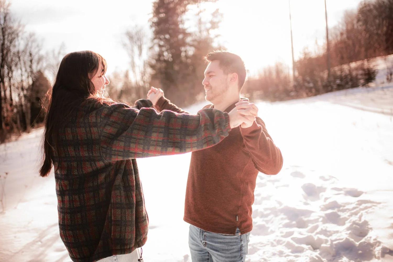 A couple dancing outdoors in the snow on a sunny winter day, holding hands and smiling at each other.