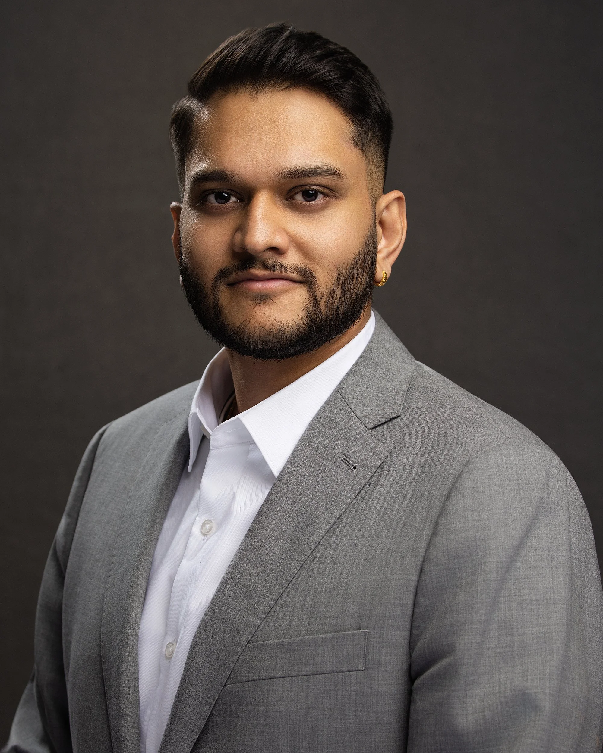 A professional man with a beard and short dark hair dressed in a light gray suit and white shirt posing against a dark background.