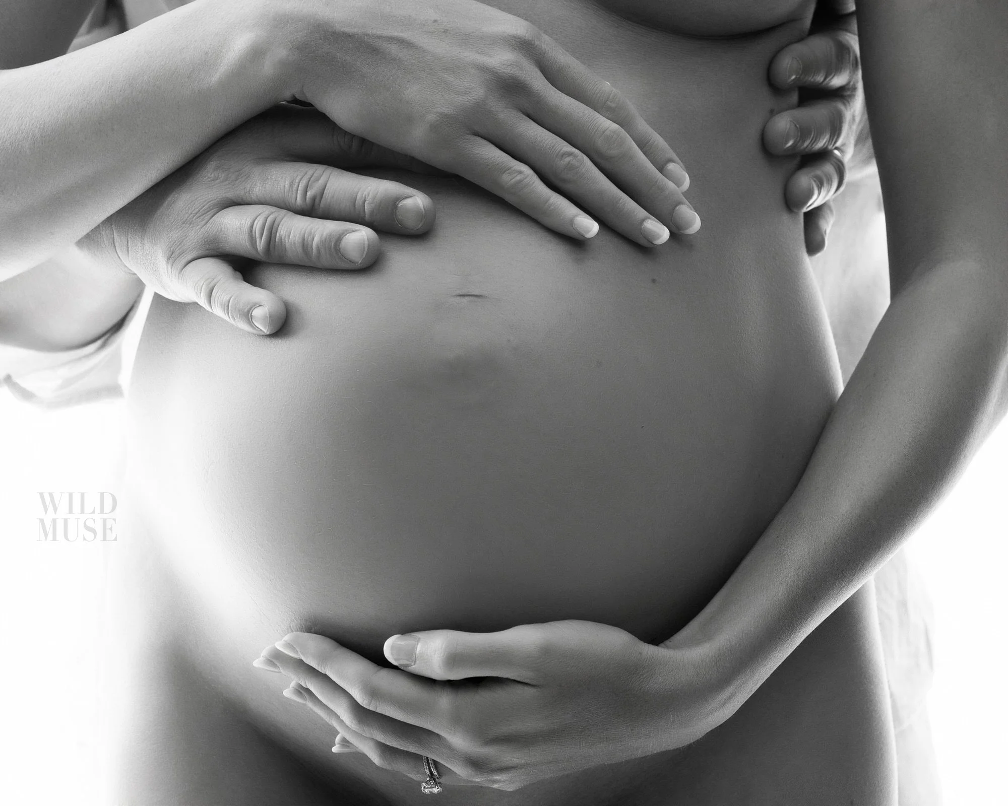 Close-up of a pregnant woman's belly with hands gently cradling it, in black and white.