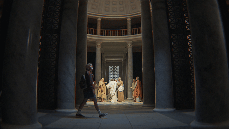 A woman walking past a group of sculptures of historical figures inside a grand, circular building with columns and a domed ceiling.