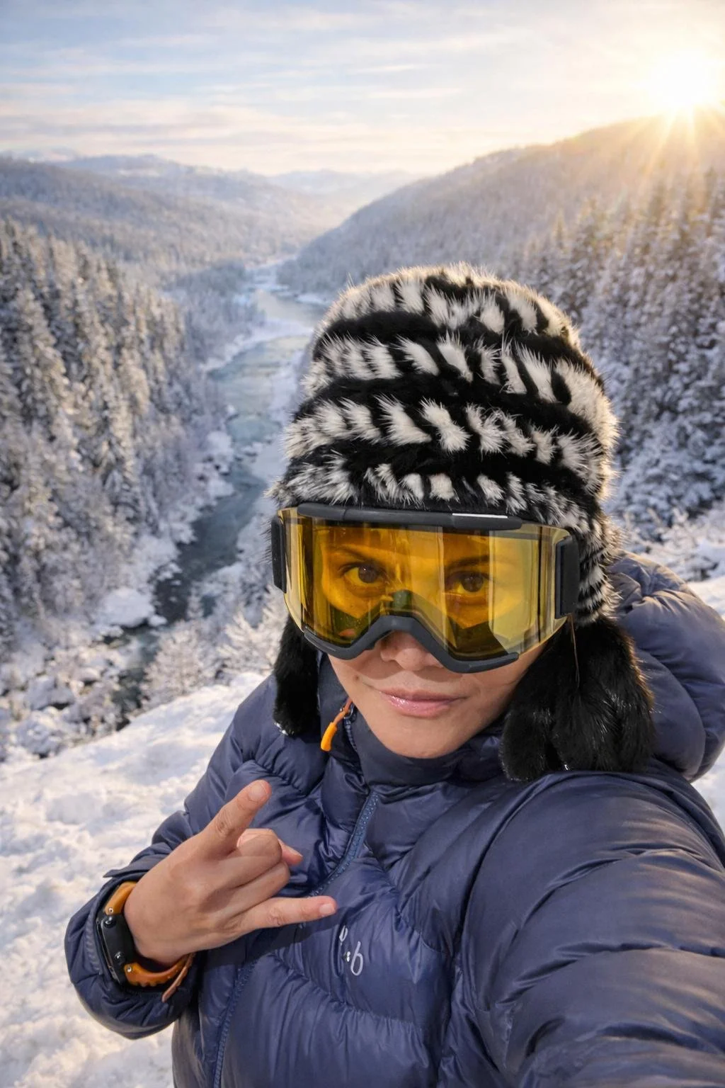 April Alfarnes taking a winter adventure selfie in Telemark, Norway, wearing ski goggles and a warm jacket with a snowy valley and river behind her.