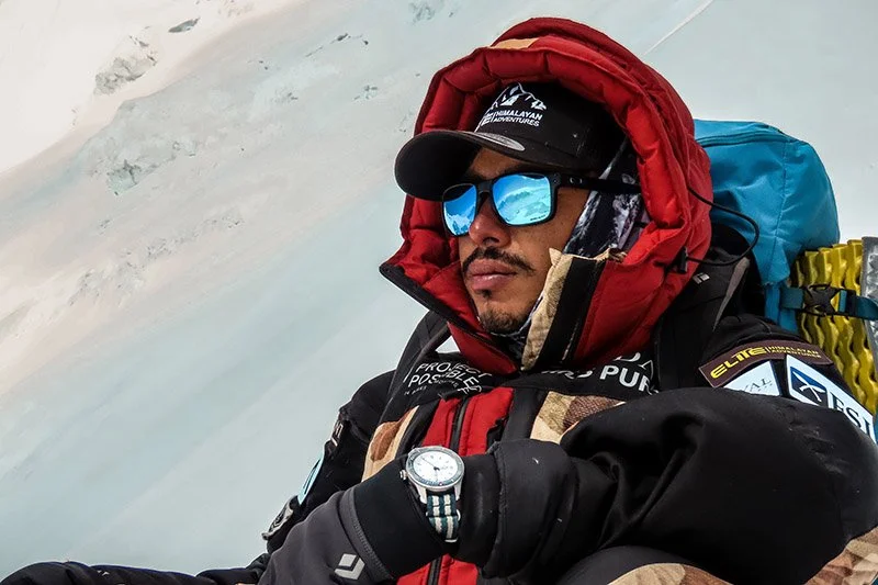 Nirmal "Nimsdai" Purja resting during a high-altitude Himalayan expedition while wearing insulated mountaineering gear and glacier sunglasses.