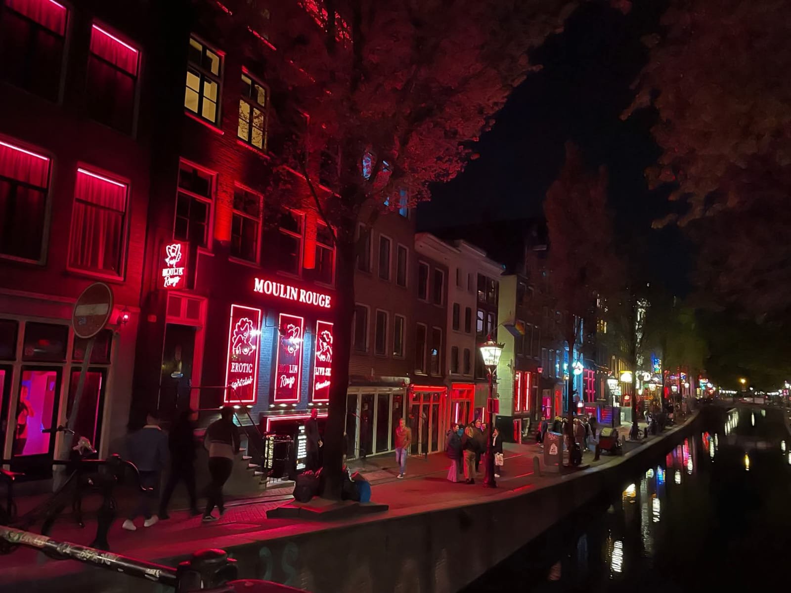 Moulin Rouge area in Amsterdam’s Red Light District illuminated in red neon as tourists walk through the vibrant nightlife corridor