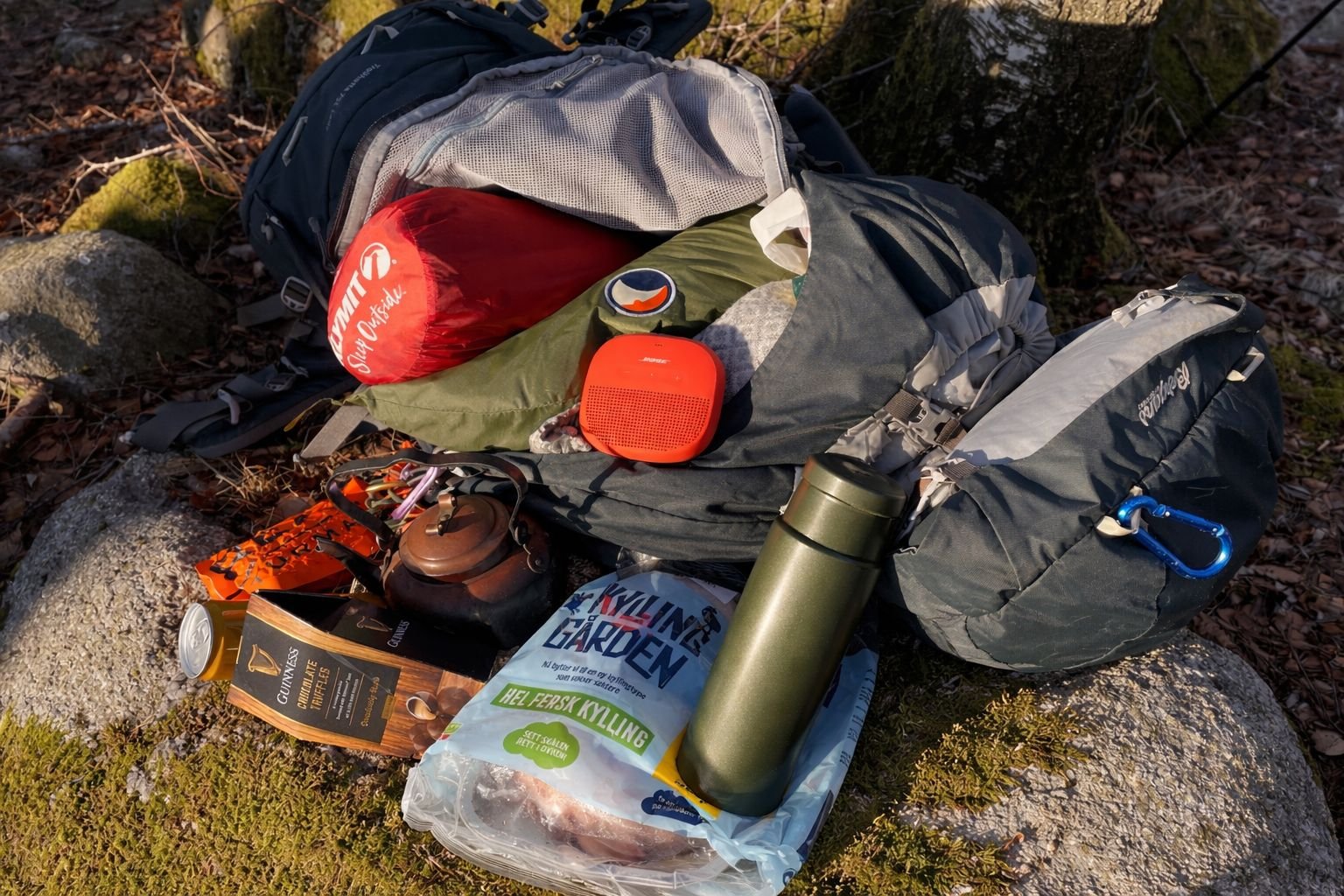 Winter camping gear including backpack, sleeping bag, stove, kettle, thermos and food supplies laid out on rock at Sviland Falls in Rogaland, Norway