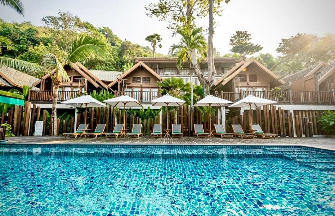 Poolside view of Ao Prao Resort in Koh Samed, with wooden villas, sun loungers, palm trees, and tropical hillside surroundings