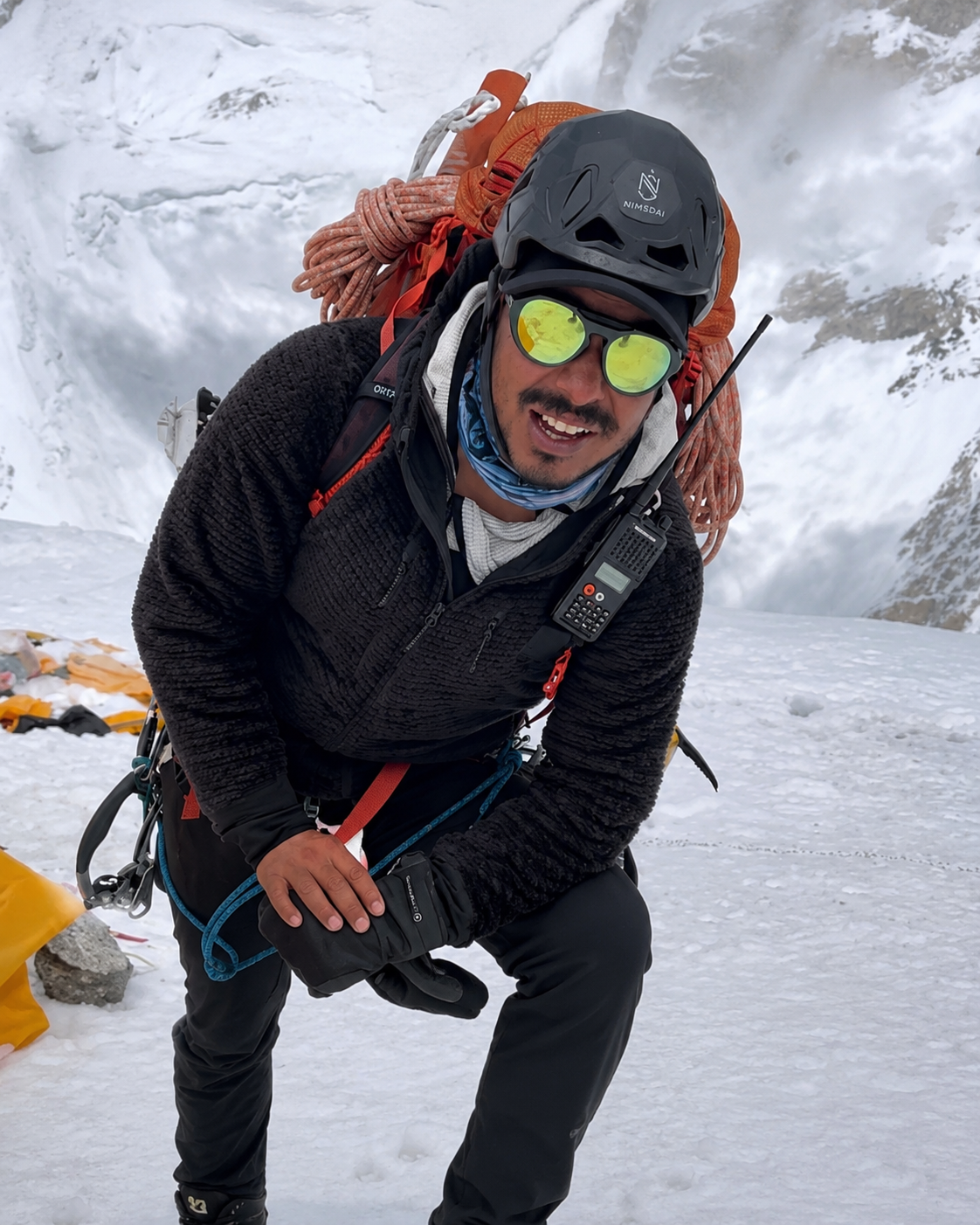Nirmal "Nimsdai" Purja during a high-altitude Himalayan expedition, wearing climbing gear and smiling while standing on snow and ice.