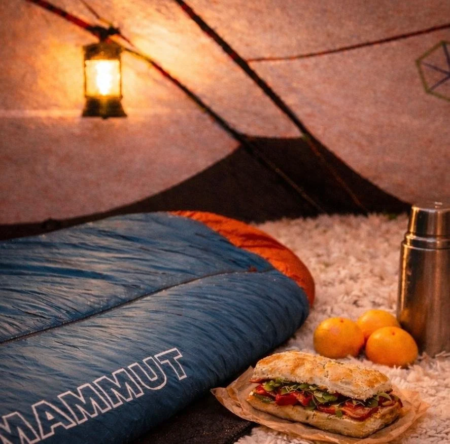 Inside April Alfarnes’ winter tent in Telemark, showing a Mammut sleeping bag, lantern glow, fresh sandwich, and camping essentials.