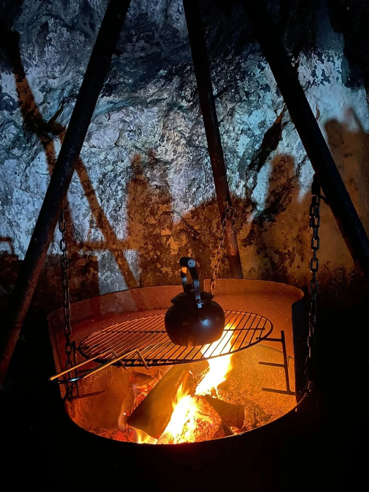 “Fire pit with a hanging kettle glowing against stone walls inside Tunnelstuo abandoned tunnel in Flekkefjord, Norway.