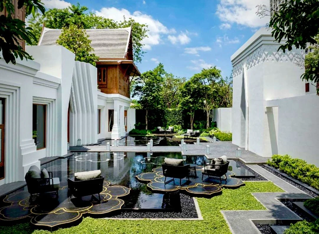 The Sukhothai Hotel in Bangkok featuring its serene courtyard oasis with reflective pools, lotus-inspired platforms, modern Thai architecture, and lush garden surroundings.
