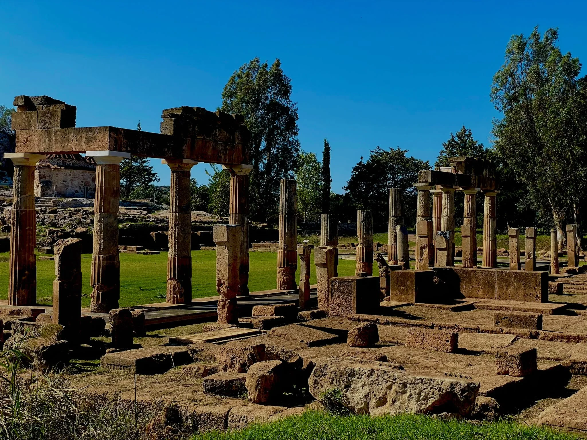 Rows of weathered stone columns and scattered blocks at the Sanctuary of Artemis in Brauron, Greece, beneath a clear blue sky.