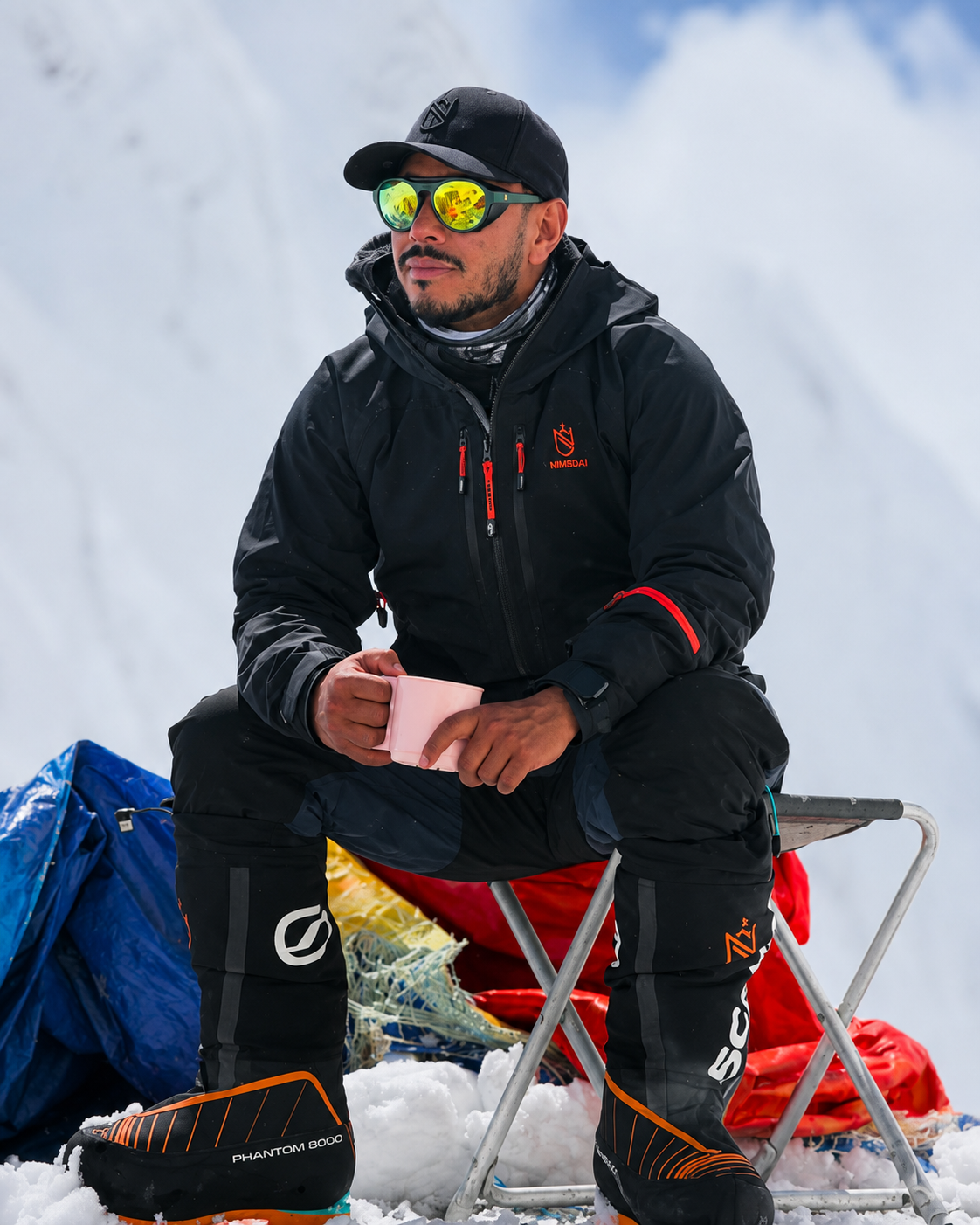 Nimsdai Purja enjoying a cup of coffee at high-altitude base camp during a Himalayan mountaineering expedition, surrounded by snow-covered peaks