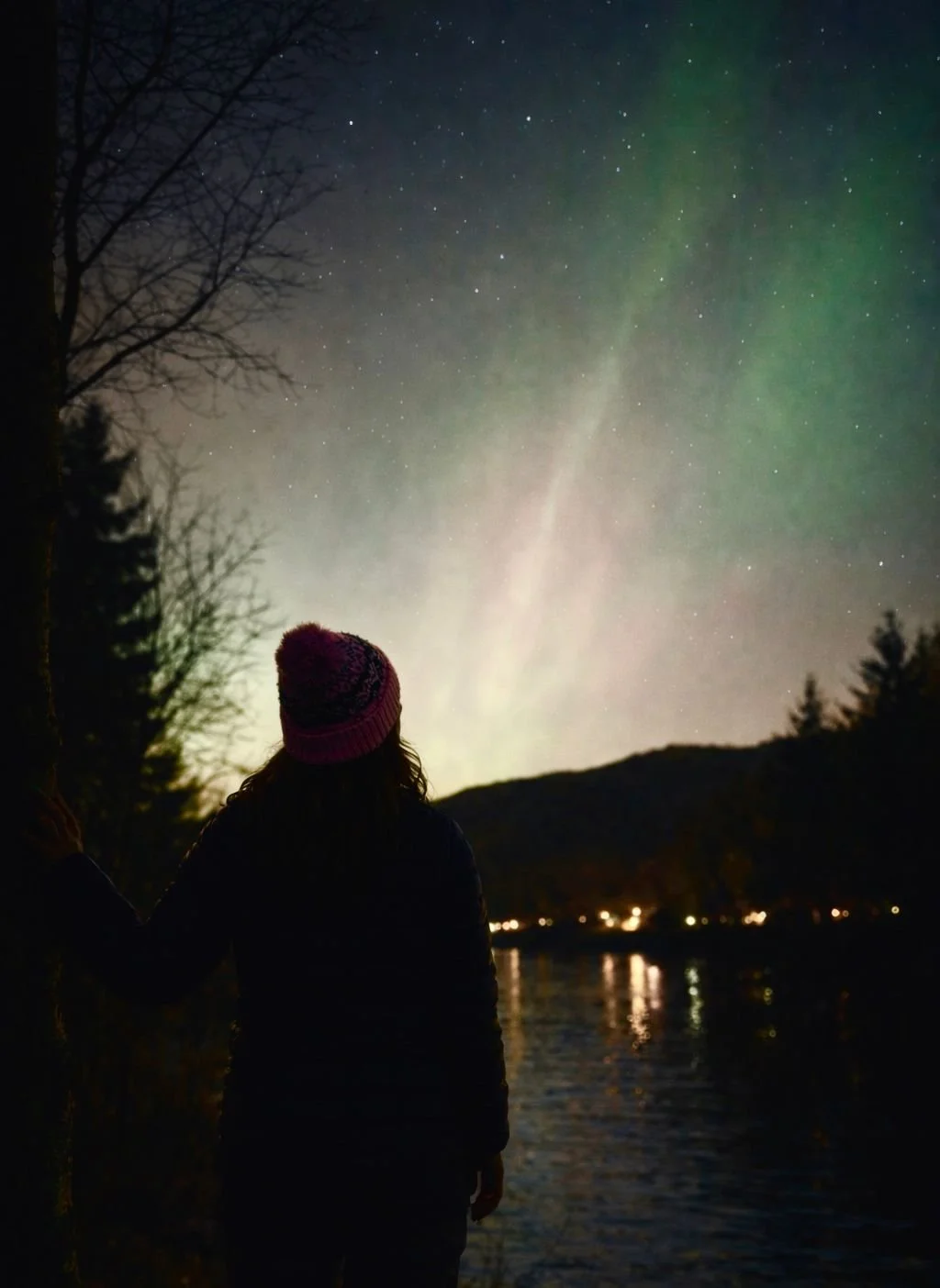 Woman standing by the water in Figgjo, Norway, watching faint traces of the Aurora Borealis