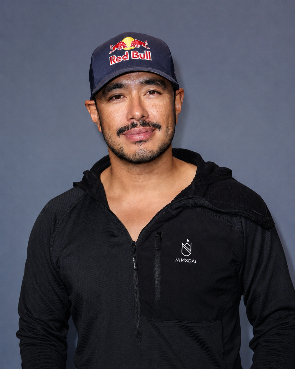 Portrait of Nimsdai Purja, elite Nepali mountaineer, wearing a Red Bull cap and Nimsdai outdoor apparel.