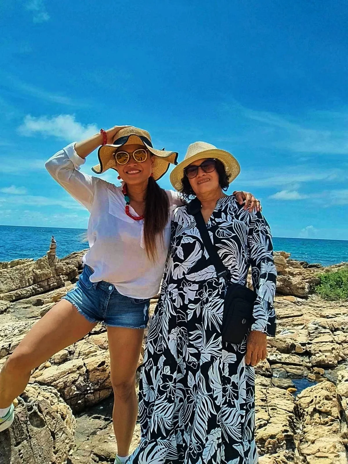 April Joy Alfarnes and her mother posing on the rocky coastline of Koh Samed, Thailand, under clear blue skies—capturing a bright tropical moment during their island tour