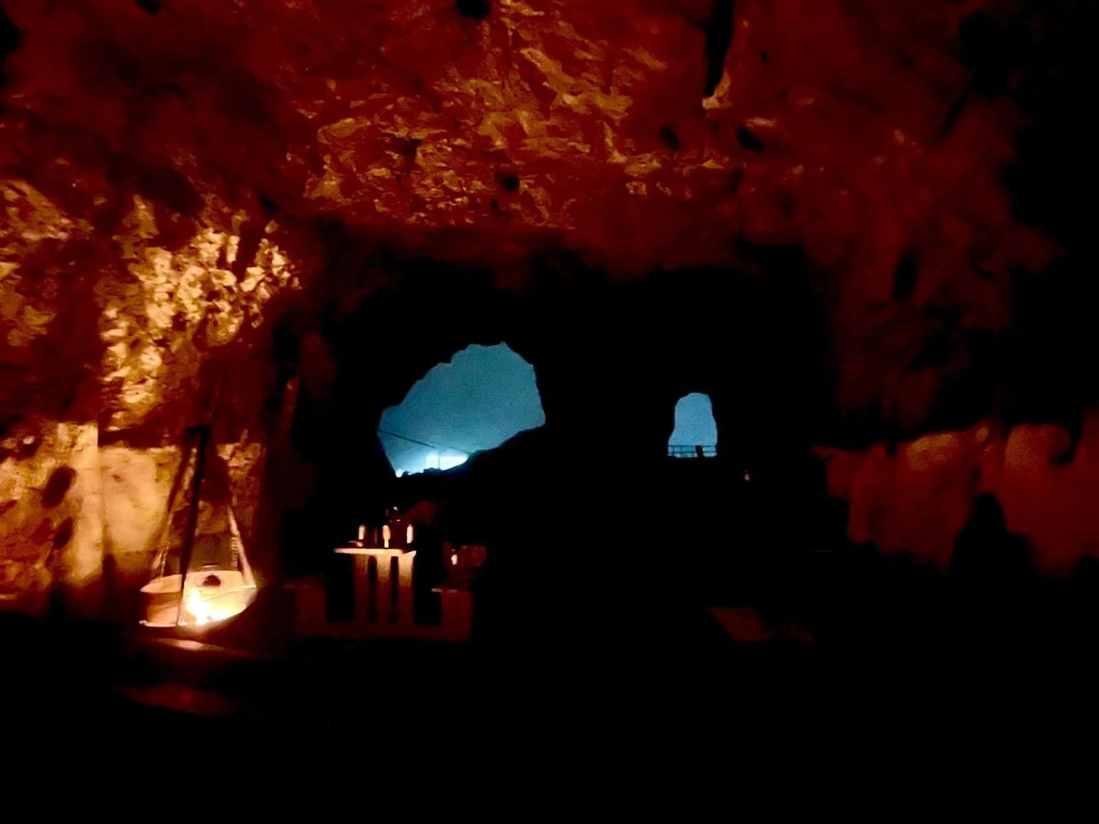 Night view inside Tunnelstuo showing firelight reflecting on rocky walls and the tunnel’s distant blue exit