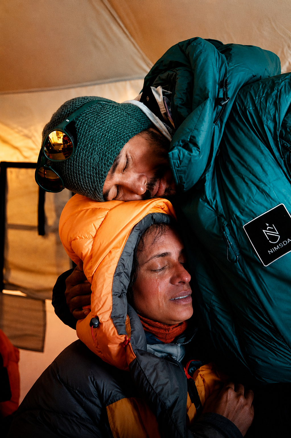 Nimsdai embraces a fellow expedition member inside a mountain tent during a Himalayan climbing expedition.