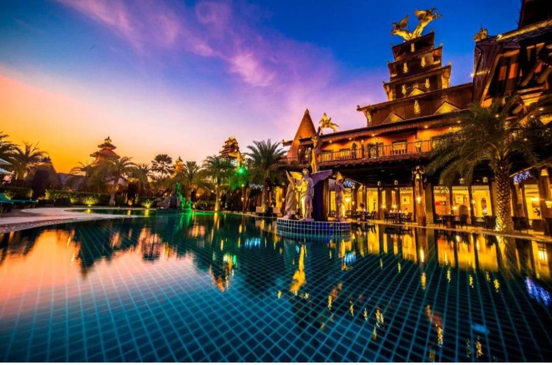 Ammata Lanta Resort in Bangkok at sunset, featuring a dramatic maximalist Thai-inspired architecture with statues and palm trees reflecting on a turquoise pool