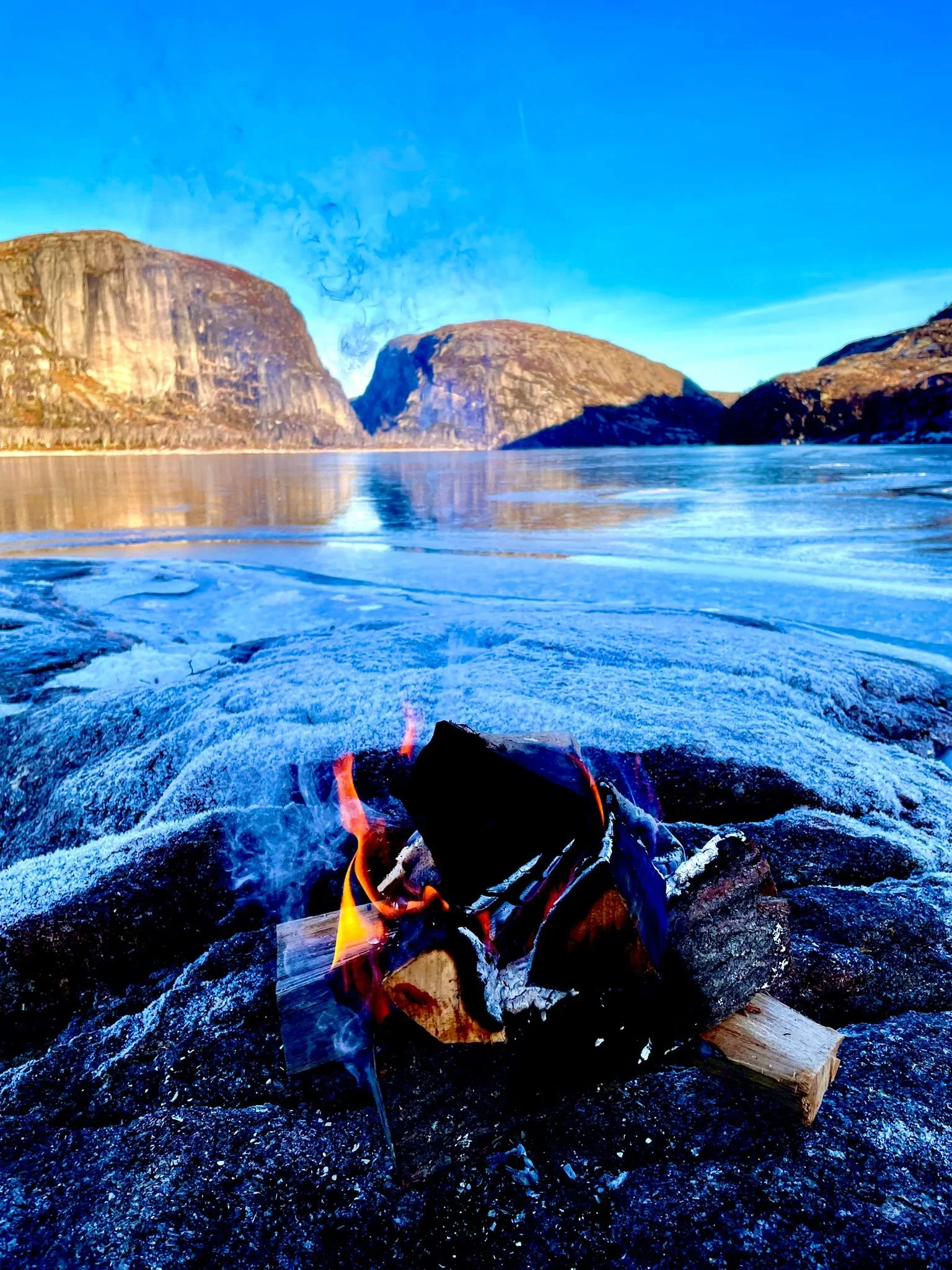 A small bonfire burning on frosty rocks beside a frozen Norwegian lake.