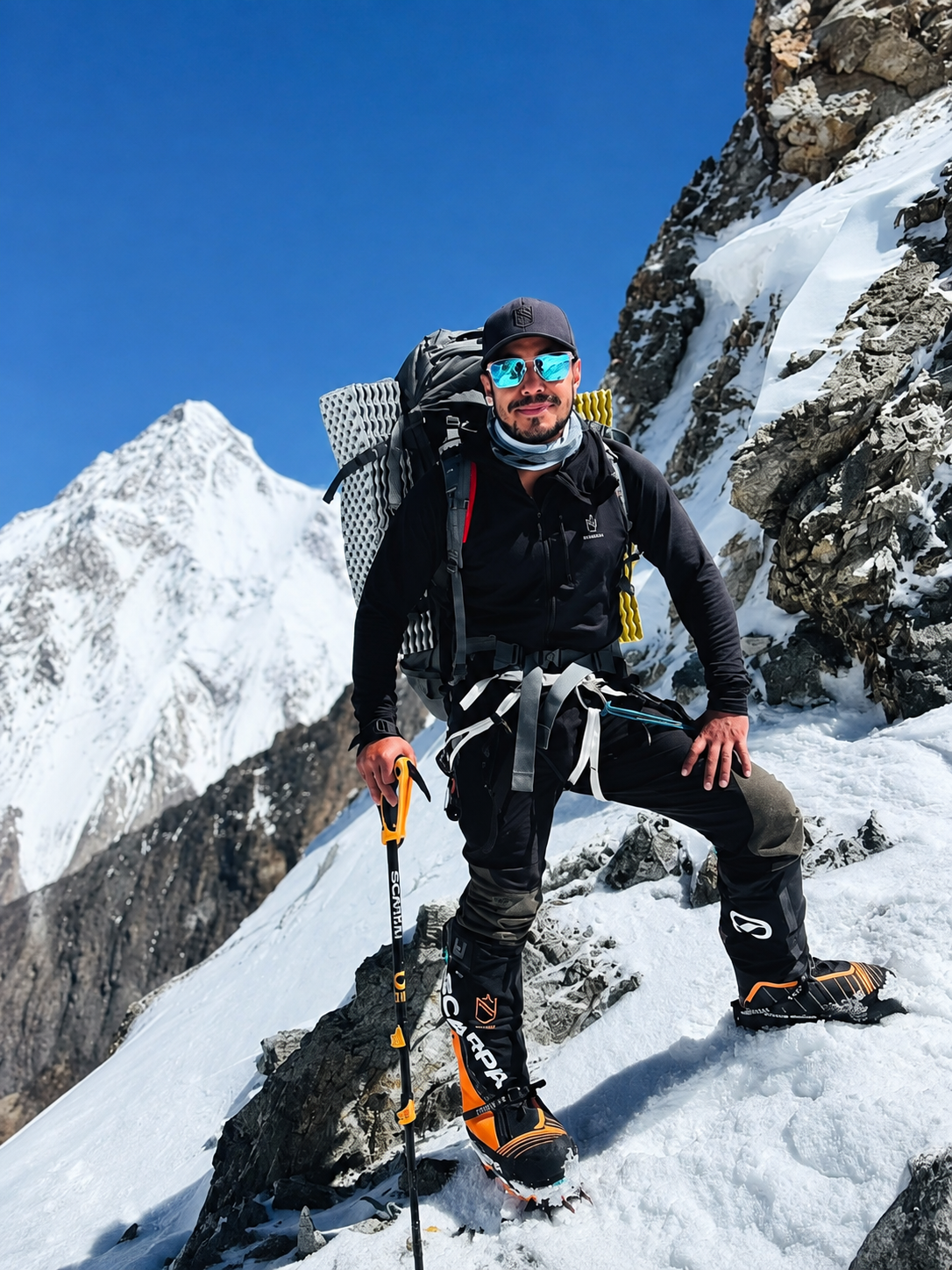 Nimsdai Purja standing on a snowy mountain ridge during a high-altitude mountaineering expedition with technical climbing equipment.