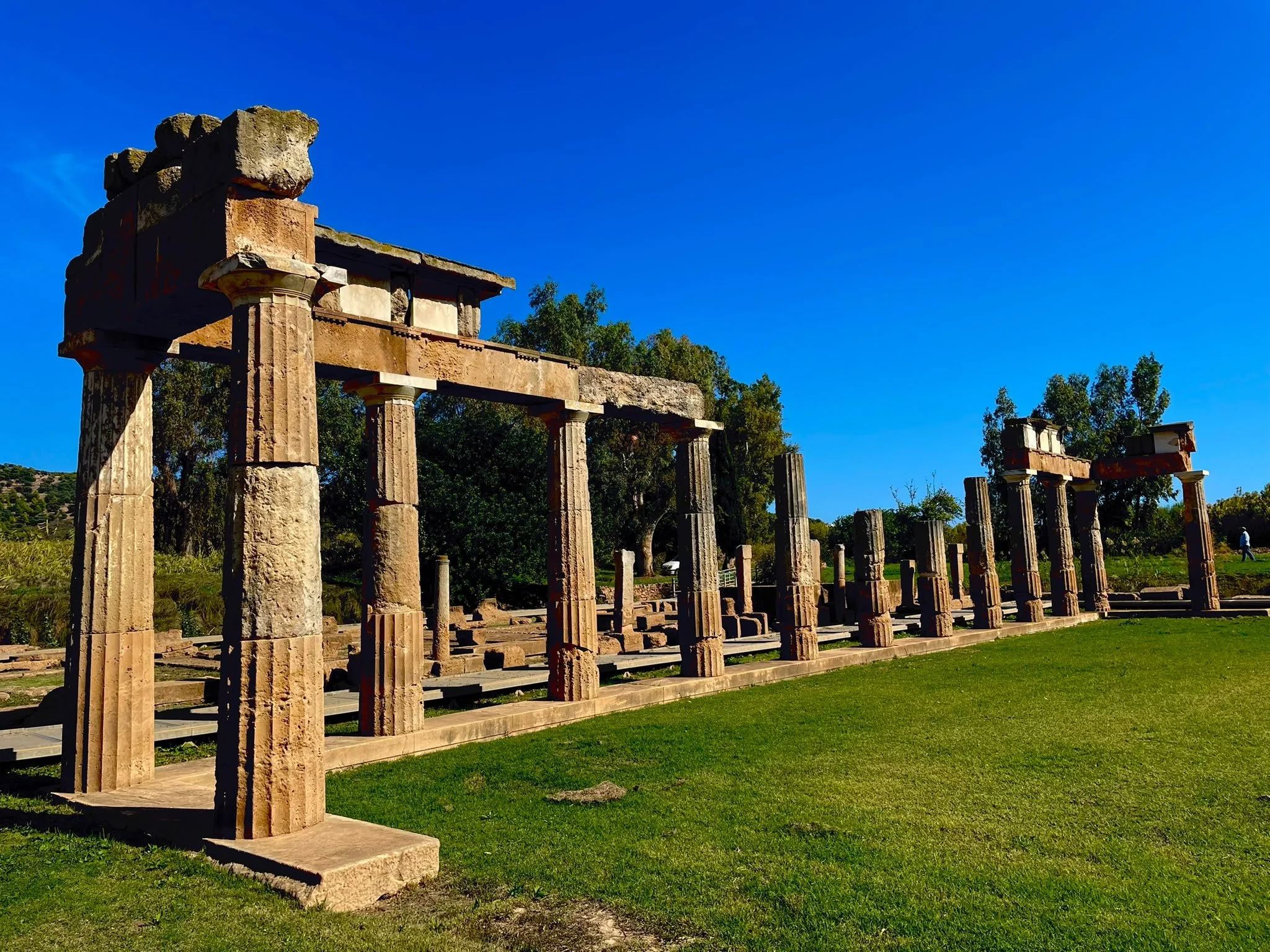 Stone columns supporting sections of lintel beside a green lawn at the Sanctuary of Artemis in Brauron, Greece.