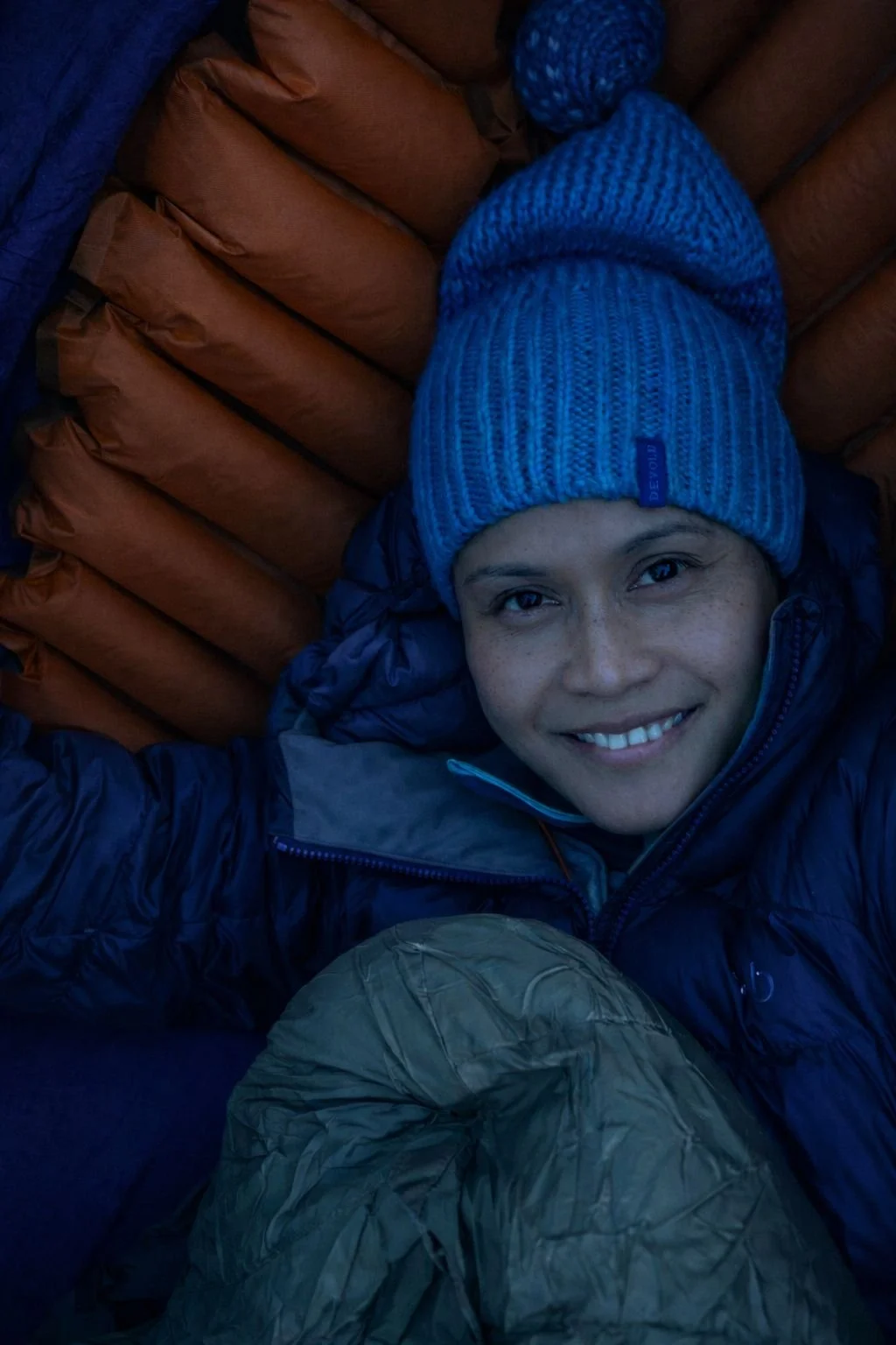 Woman resting inside a hammock at dusk wearing winter clothing, using a Klymit Insulated Hammock V sleeping pad and military-grade sleeping bag during winter camping in Norway.