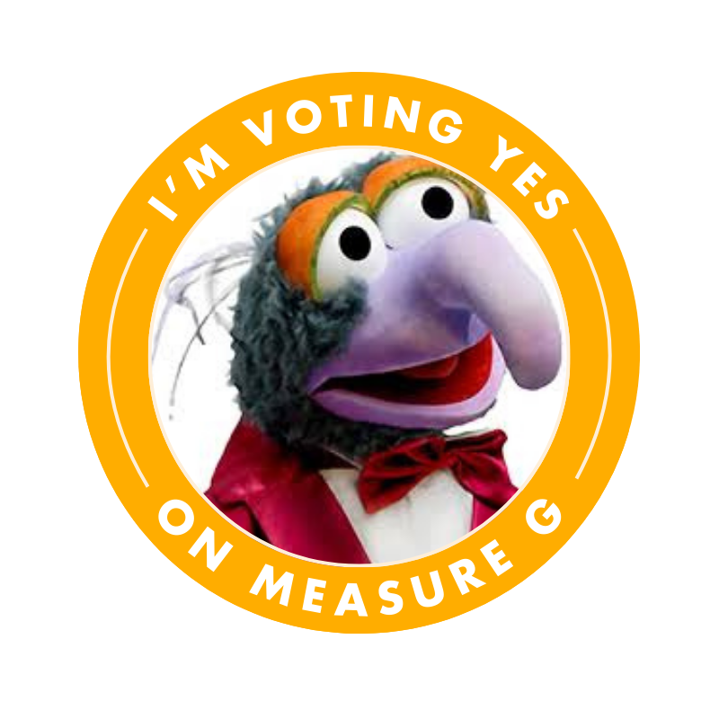 A puppet character with three eyes, a large nose, and a red bow tie, wearing a red jacket, inside a yellow circular badge that says 'I'm voting yes on Measure G'.