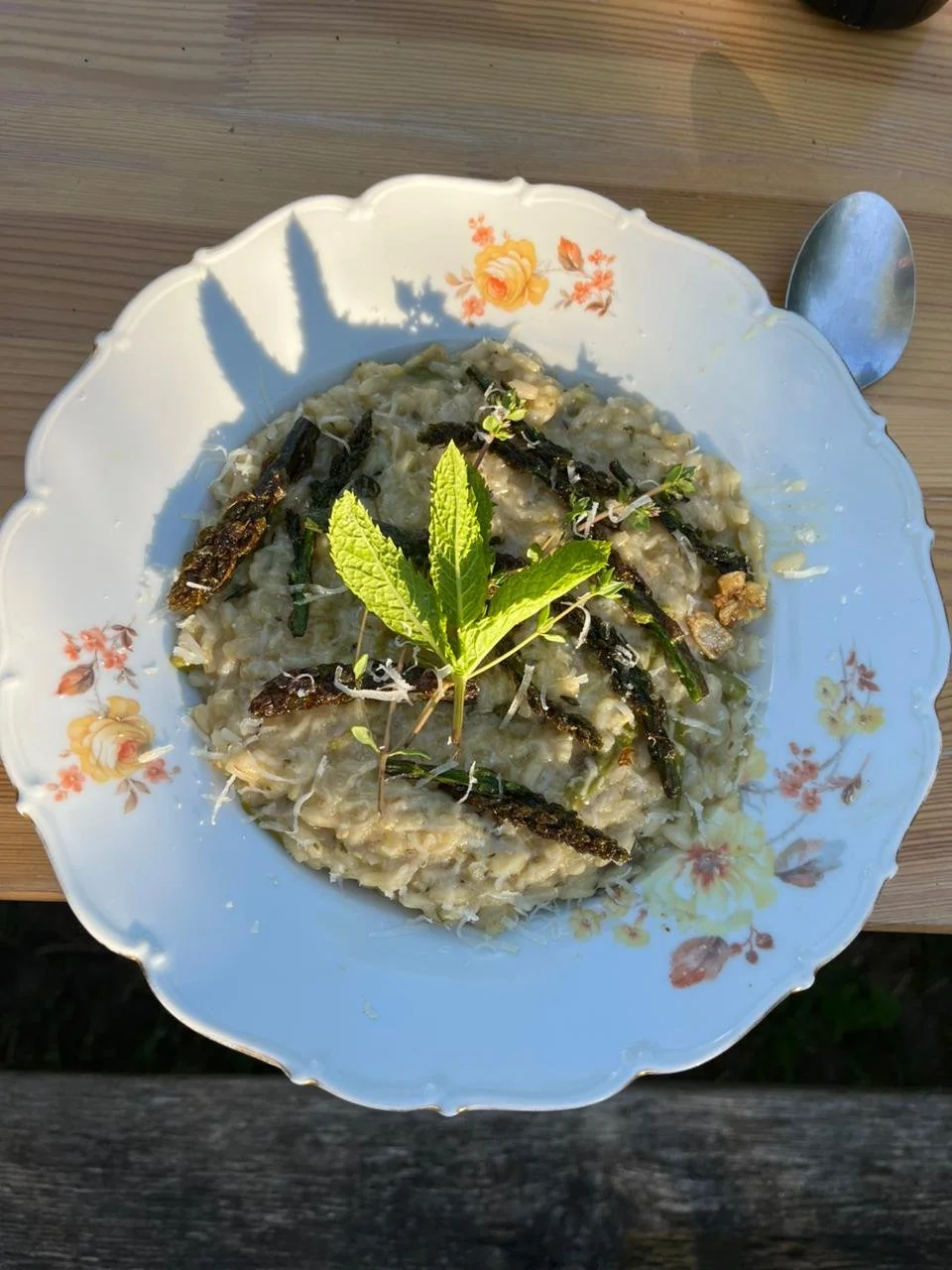 A plate of risotto garnished with fresh mint leaves and asparagus, served on a floral porcelain plate.
