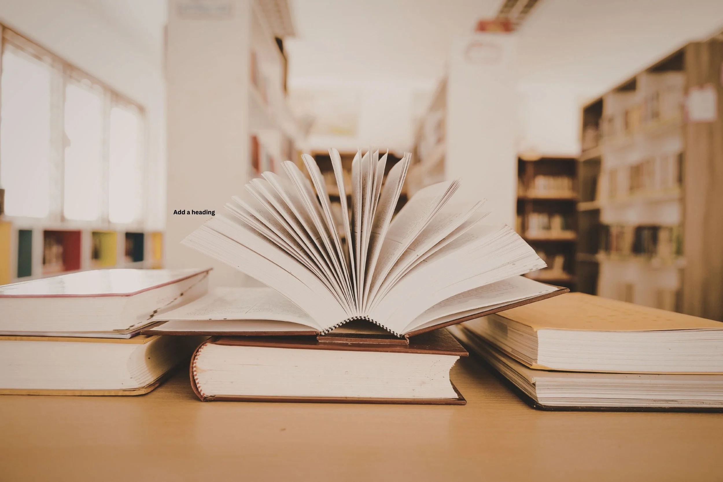 Open book with fanned pages on a wooden table inside a library, with bookshelves in the background.
