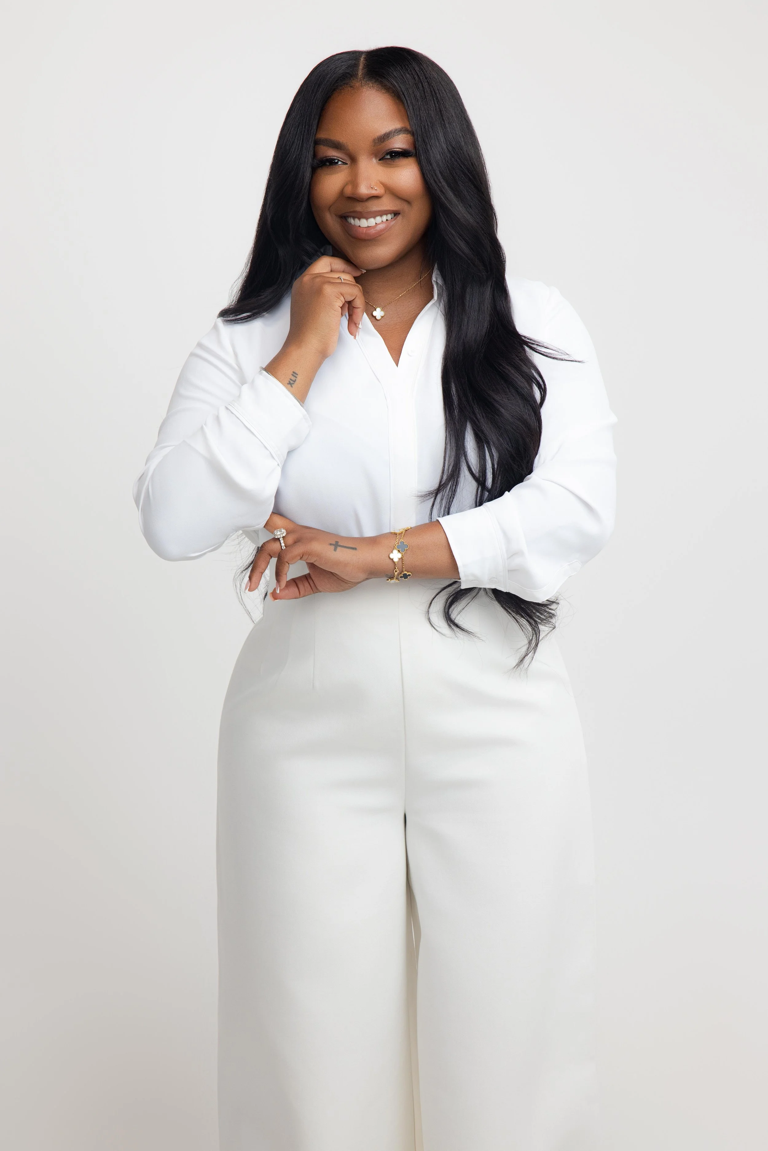 A woman with long black hair, wearing a white outfit, smiling and posing against a plain white background.