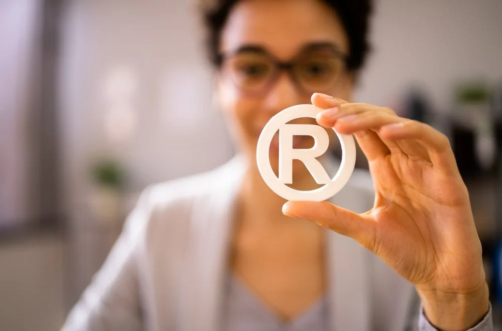Person holding a copyright symbol (©) in focus with blurred person in background.